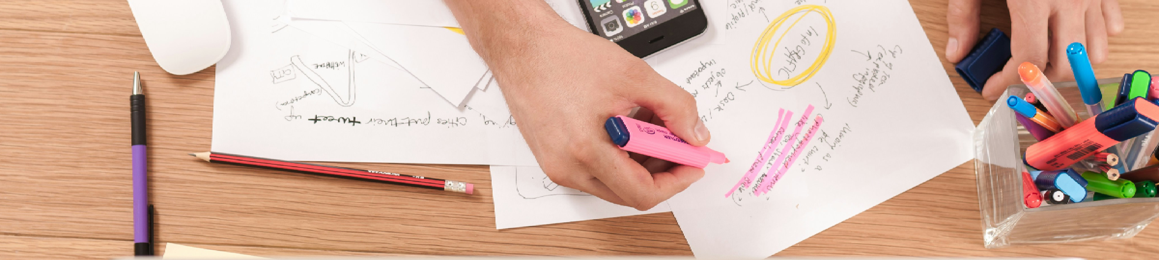 A photo of someone editing hand-written notes, highlighting texts and working across their phone, paper, and computer