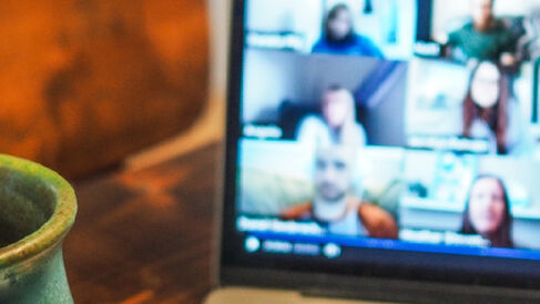 A cup of coffee is shown next to a laptop during an online meeting