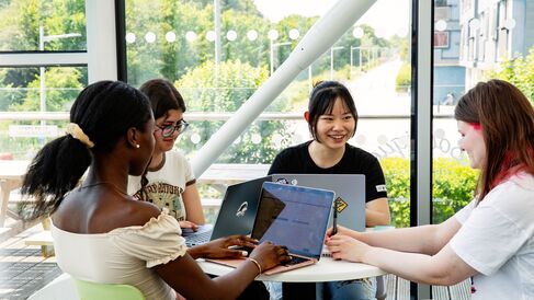 A group of University of Cambridge students working on laptops around a small table in front of a large window at the West Café. Copyright: University of Cambridge (June 2023)