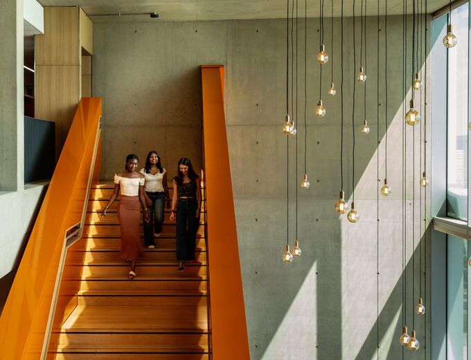 A group of University of Cambridge students walking down the orange stairs and chatting at the West Hub. Copyright: University of Cambridge (June 2023)